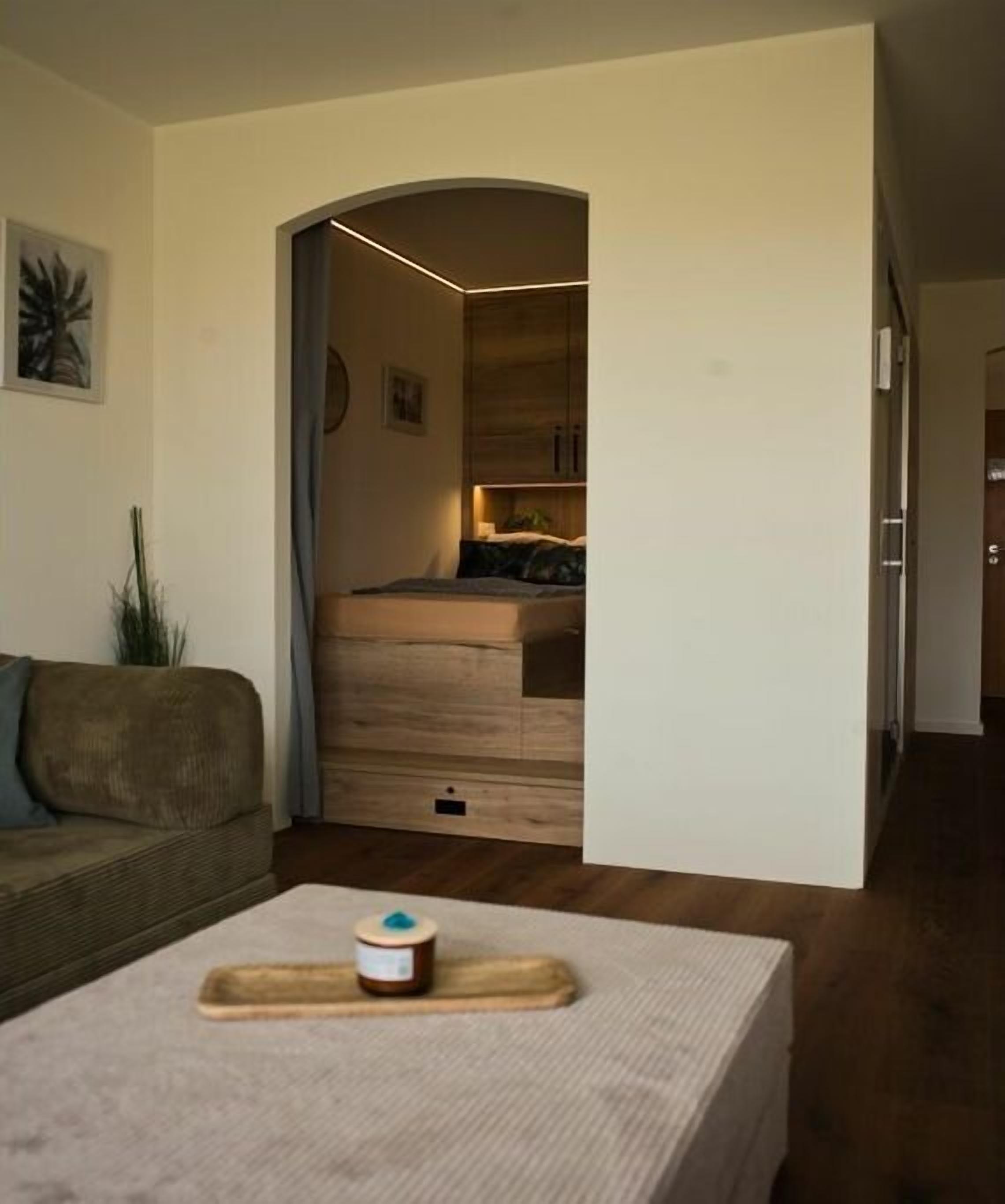 Un intérieur moderne avec un canapé, une petite table surmontée d’un récipient et, au fond, un meuble en bois.