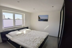 Ein Schlafzimmer mit einem Bett, einem Fenster mit Jalousien, einem Bild an der Wand und einer Tür.