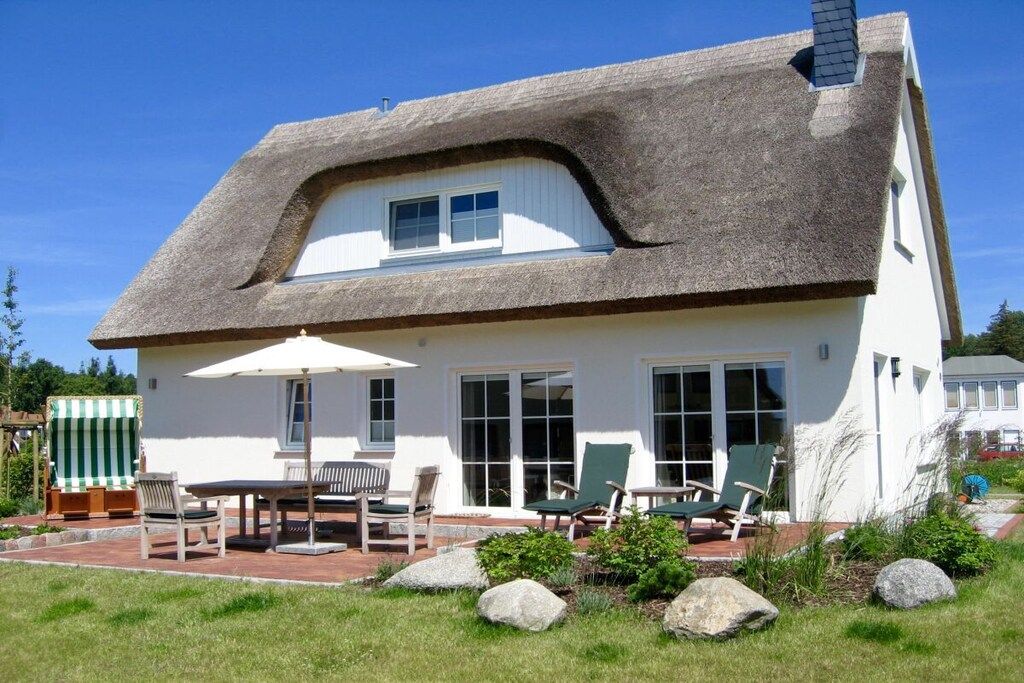 Una casa con techo de paja, un patio con mobiliario exterior y un jardín bien cuidado.