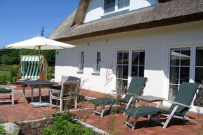 A house with a thatched roof, a patio with outdoor furniture, and a view of greenery. - Holiday home in Breege with swimming pool (Breege)