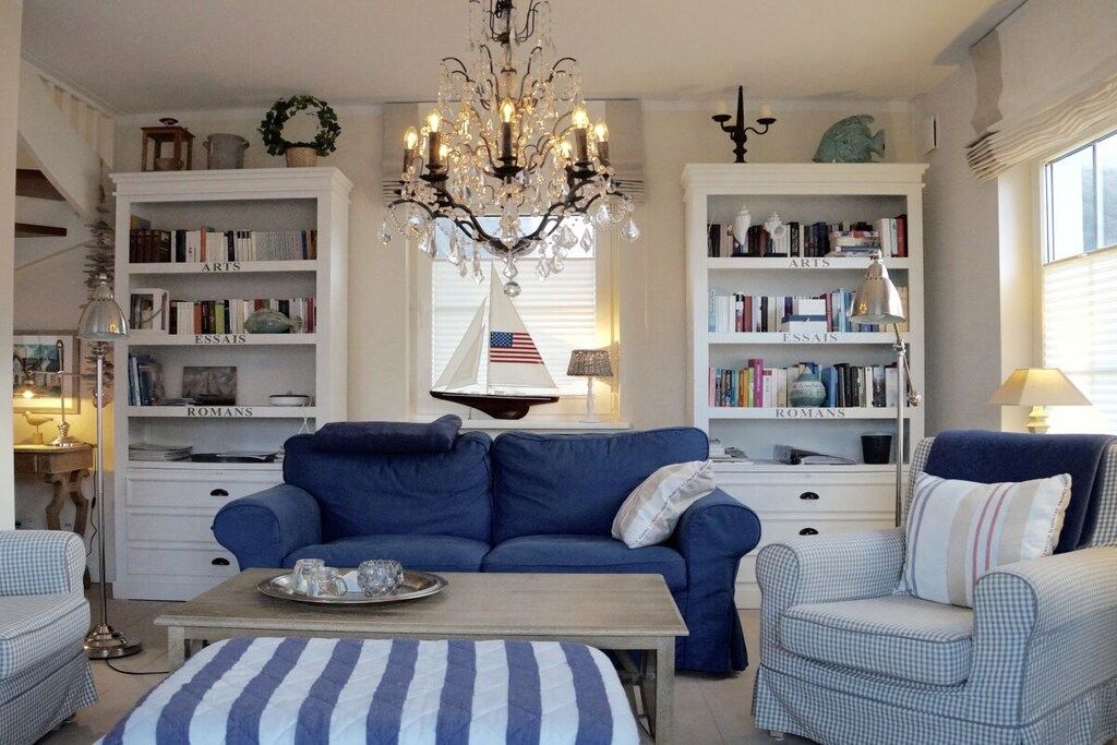 Ein Wohnzimmer mit einem blauen Sofa, einem passenden Sessel, einem Couchtisch und Bücherregalen mit den Aufschriften 'ARTS' und 'ROMANS'.