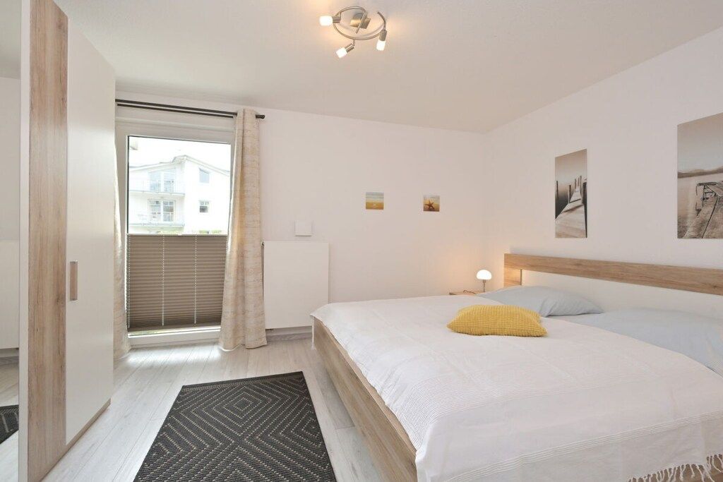 Een slaapkamer met een bed, nachtkastje, lamp en raam met gordijnen.
