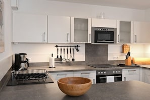 A modern kitchen with white cabinets, a black oven, and a wooden bowl on the counter. - Holiday apartment with 1 bedroom (Breege\/ Juliusruh OT Juliusruh)