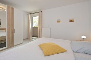 A bedroom with a bed, a nightstand, a lamp, and a window with curtains. - Holiday apartment with 1 bedroom (Breege\/ Juliusruh OT Juliusruh)