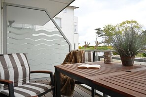 A wooden deck with a chair and a table, a book, a potted plant, and a glass wall with a wavy pattern. - Holiday apartment with 1 bedroom (Breege\/ Juliusruh OT Juliusruh)