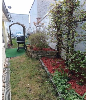 Un patio trasero con una parrilla, una jardinera de piedra con acolchado rojo y una planta trepadora.
