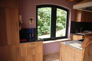 A kitchen with wooden cabinets, a coffee maker, and a window with a view of greenery. - Holiday home in Jabel with swimming pool (Jabel)