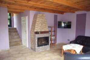 A living room with a stone fireplace, a wooden ceiling, a black leather sofa, and a television mounted on the wall. - Holiday home in Jabel with swimming pool (Jabel)