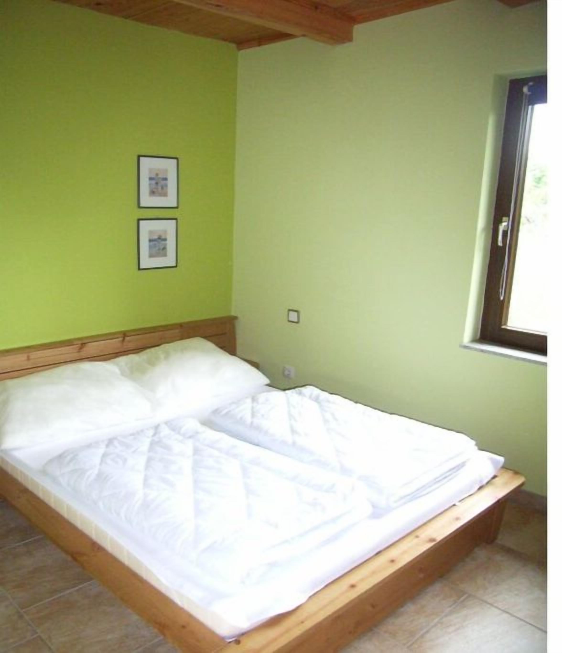 Een eenpersoonsbed met houten frame en wit beddengoed in een kamer met groene wanden en een raam.