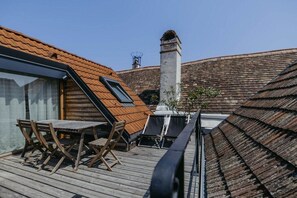 A wooden deck with a table and chairs, a chimney, and a sloped roof. - Streckhof Stiefelgasse attic (Purbach am Neusiedler See)