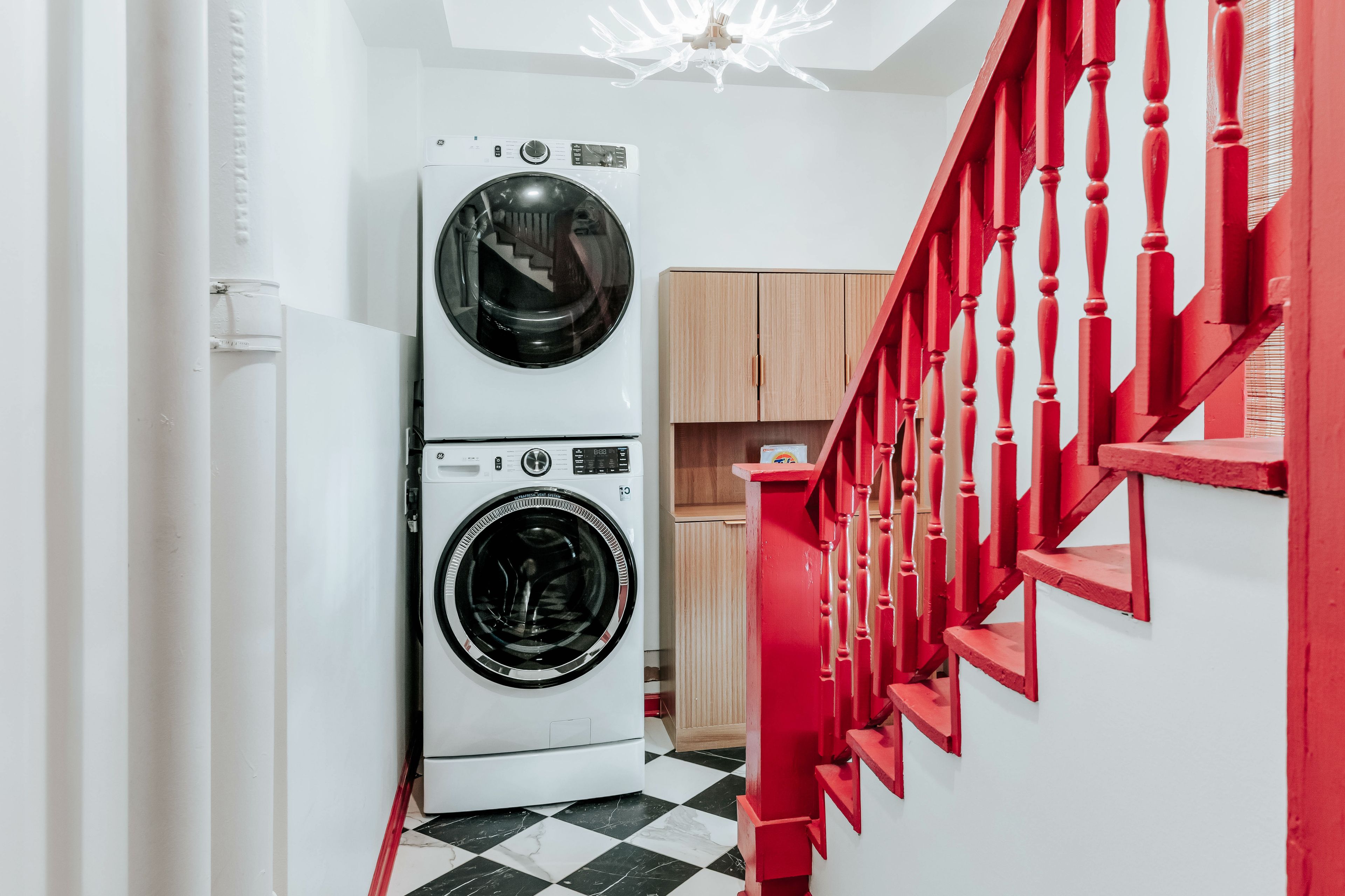 A laundry area with stacked washing machines and a red staircase.
