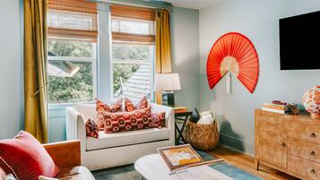 A room with a sofa, a table, a lamp, a fan, and a television on the wall.