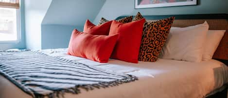 A neatly made bed with a striped throw, a variety of pillows, and a painting on the wall.