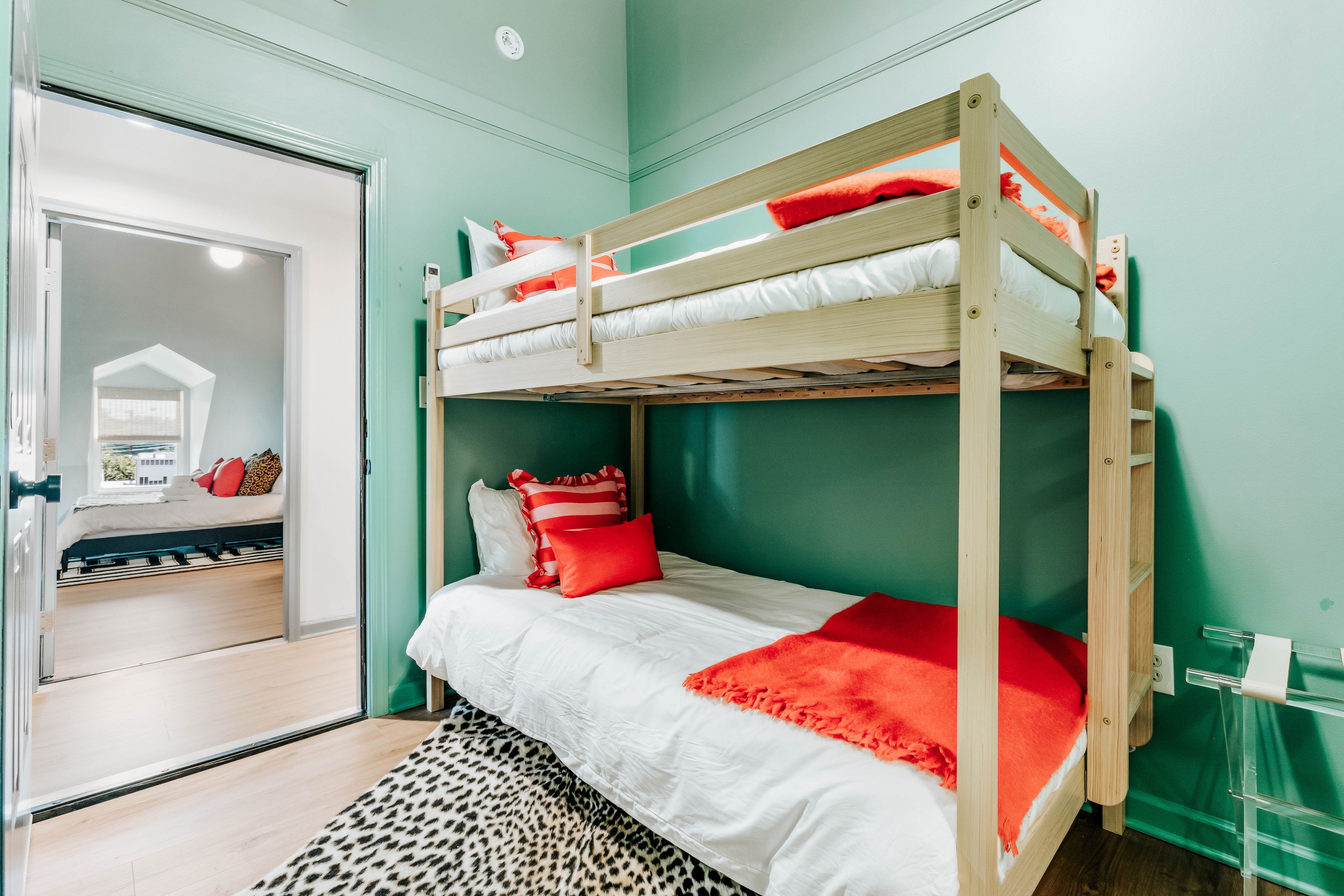 Ein Stockbett mit roter und weißer Bettwäsche, einem Leopardenmuster-Teppich und Blick auf einen Raum mit Tür und Fenster.
