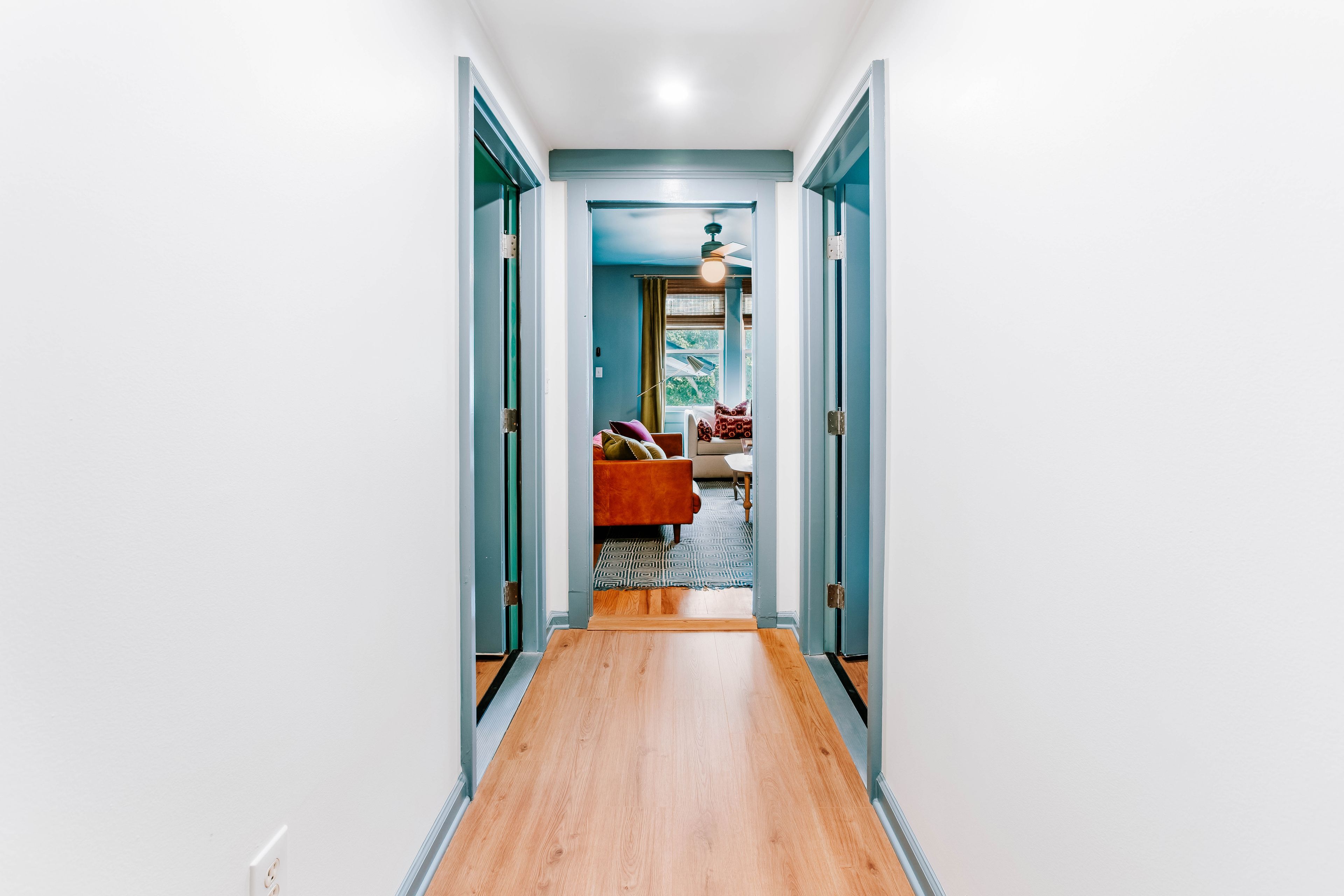 A hallway with a wooden floor leading to a room with a red sofa and patterned rug.