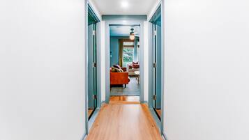 A hallway with a wooden floor leading to a room with a red sofa and patterned rug.