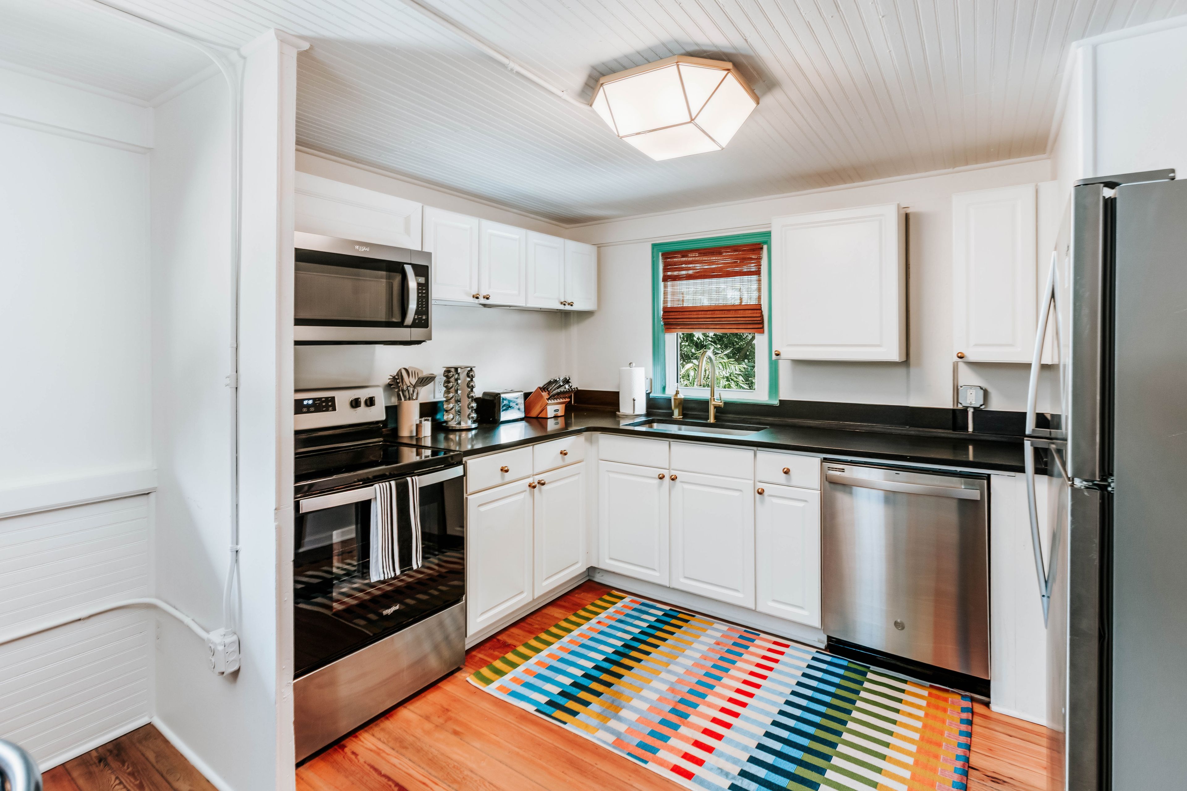 A modern kitchen with white cabinets, stainless steel appliances, and a colorful striped rug.