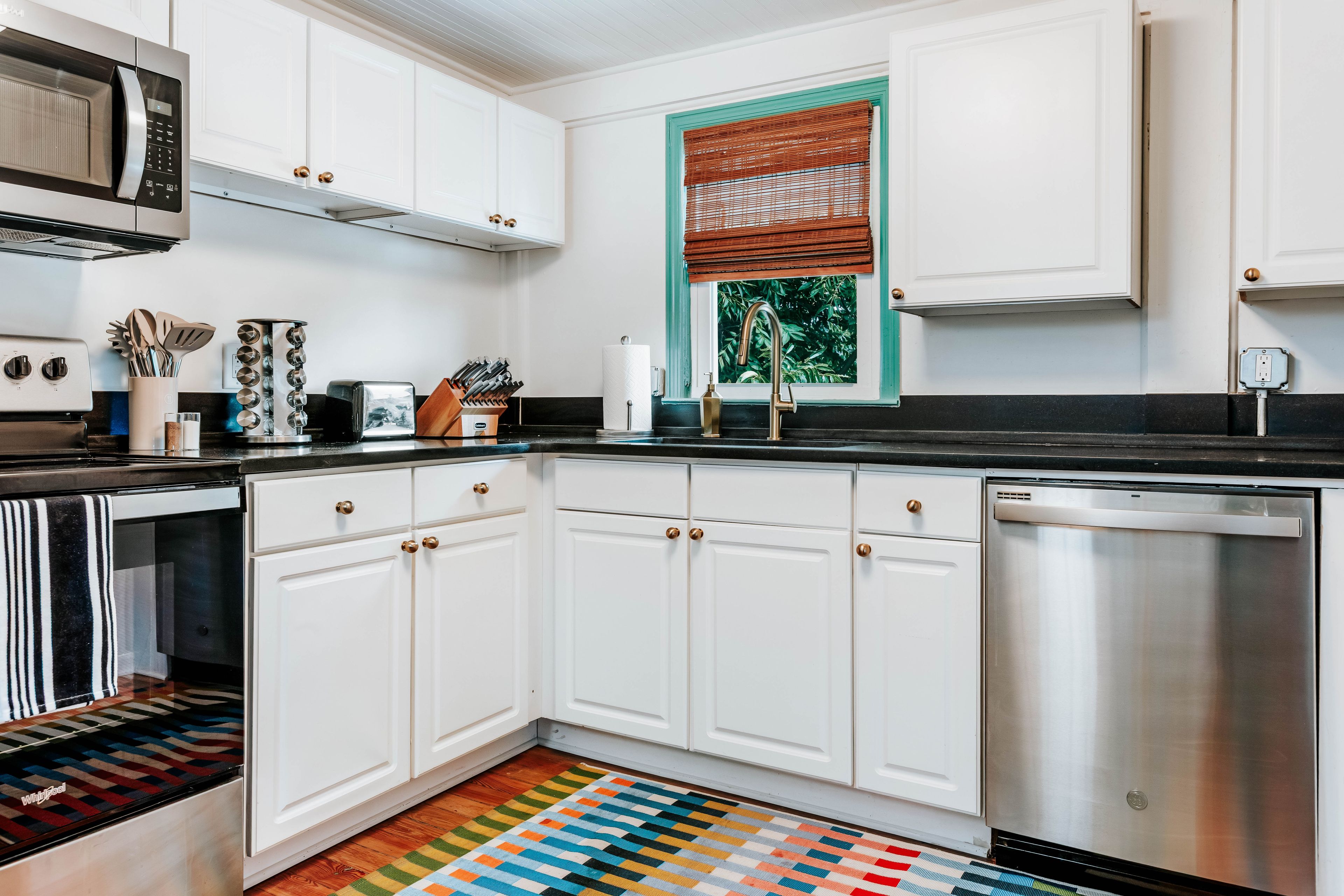 A modern kitchen with white cabinets, stainless steel appliances, and a colorful striped rug.
