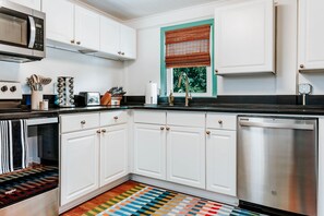 Una cocina moderna con armarios blancos, electrodomésticos de acero inoxidable y un tapete colorido a rayas.