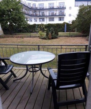 Ein Balkon mit einem runden Glastisch und zwei Stühlen, mit Blick auf ein Gebäude mit mehreren Balkonen.