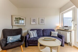 Un salon comprenant un fauteuil foncé, un canapé, une petite table ronde et un meuble avec des portes en verre.
