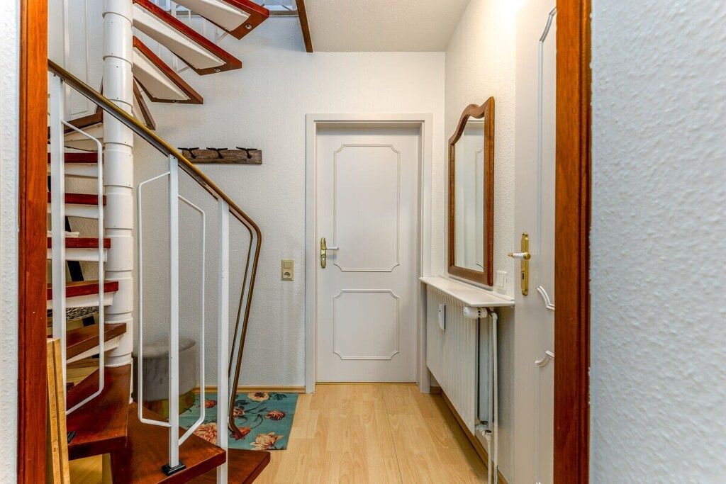 A narrow hallway with a wooden staircase on the left, a white door at the end, and a radiator on the right.