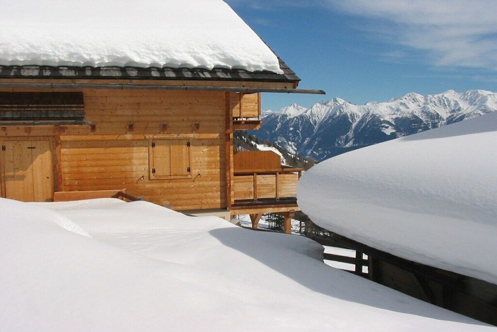 Eine Holzhütte mit verschneitem Dach und Blick auf schneebedeckte Berge.