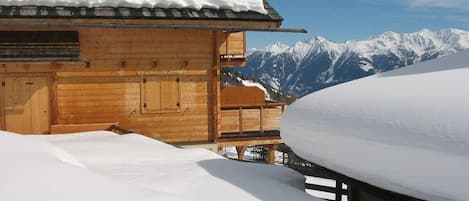A wooden chalet with a snow-covered roof and a view of snow-capped mountains.