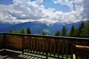 Eine Holzterrasse mit Blick auf schneebedeckte Berge und grüne Bäume.