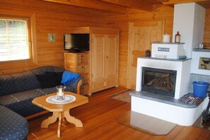 Ein Interieur einer Holzhütte mit einer Couch, einem Fernseher, einem Kamin und einem kleinen Tisch mit einer Kerze.