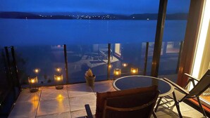 Terraço com vista para a água, mesa redonda e várias cadeiras.