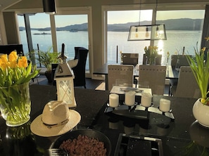 A dining area with a view of a body of water, a table set with candles, and a vase of yellow flowers.