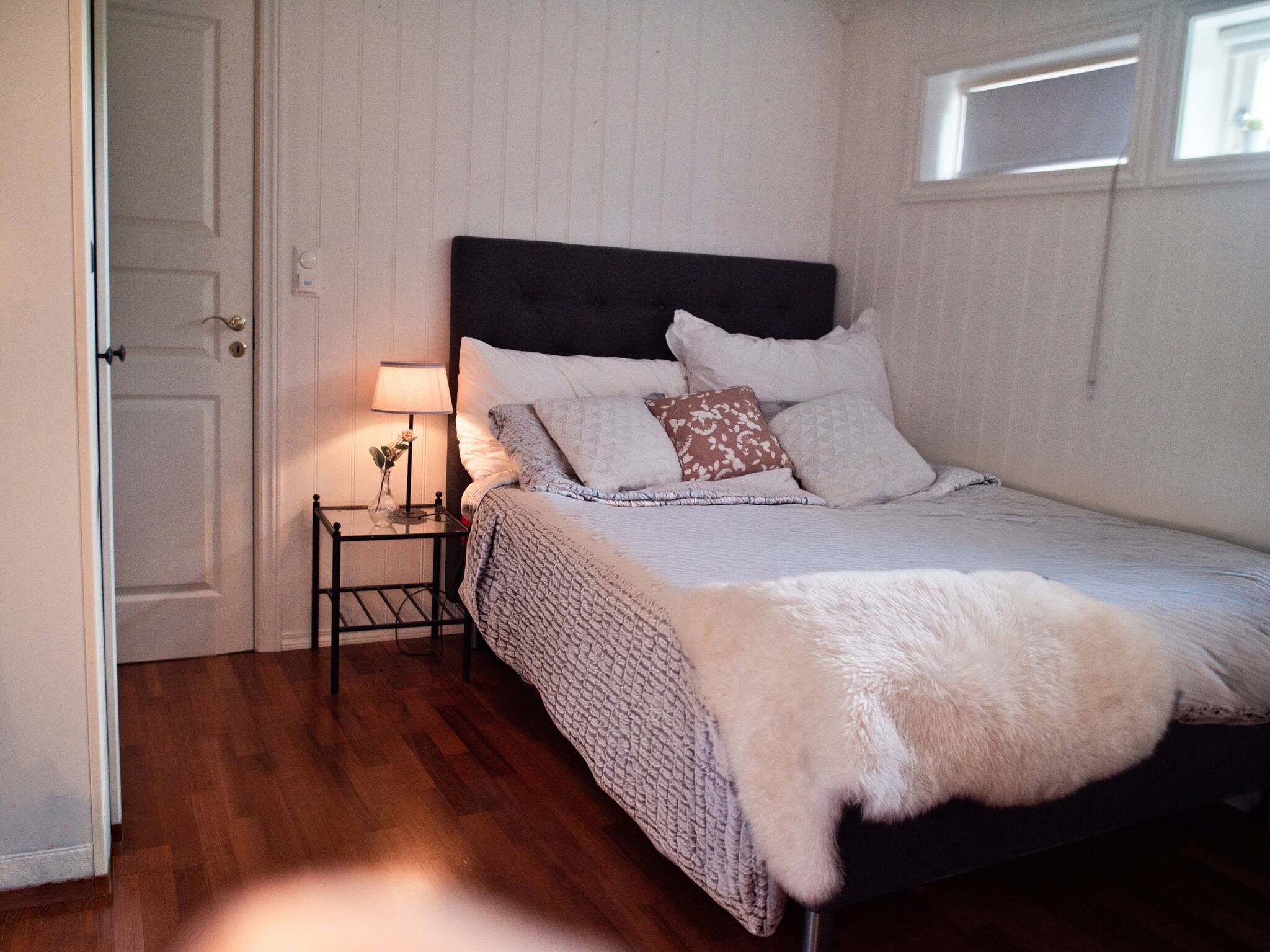 A bedroom with a bed, a bedside table with a lamp, and a door.