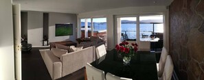 Una sala de estar con sofá, una mesa de centro y televisor. Hay un balcón con vistas al mar.