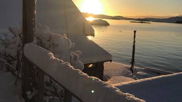 A snow-covered balcony with a view of a calm lake and distant mountains during sunset.