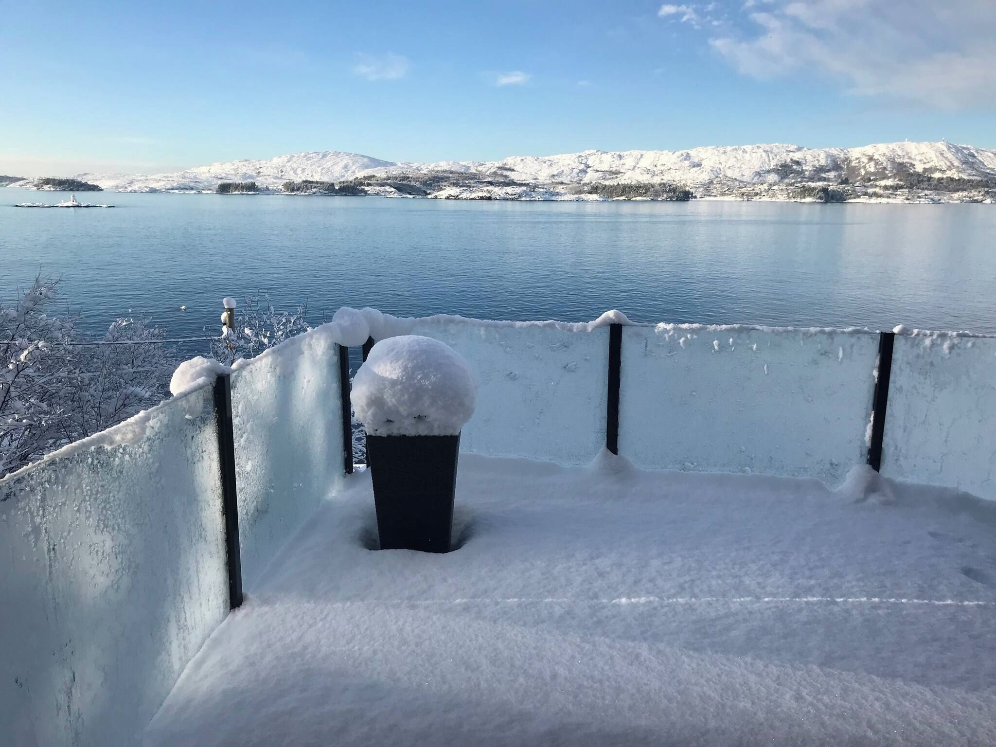 A snow-covered balcony with a view of a lake and mountains.