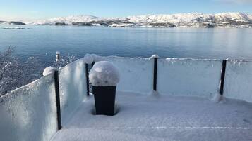 A snow-covered balcony with a view of a lake and mountains.