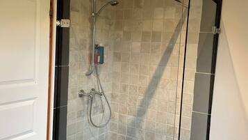 A glass-enclosed shower with a handheld showerhead and a wall-mounted faucet, set against a tiled wall with a door on one side.