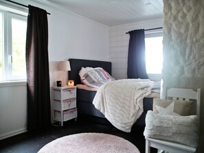 A bedroom with a bed, bedside table, lamp, and a window with curtains.