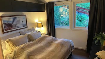 A hotel room with a bed, a nightstand with a lamp, a framed picture on the wall, and a window with curtains.