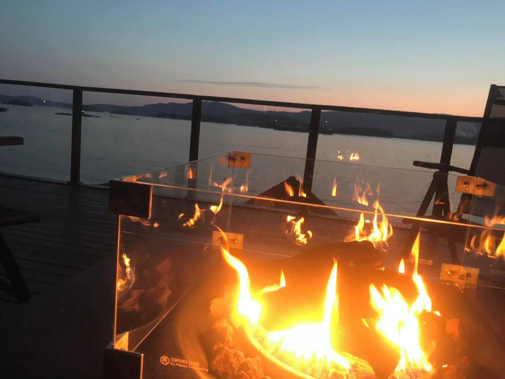 A glass-top table with a fire feature, overlooking a body of water and distant land.