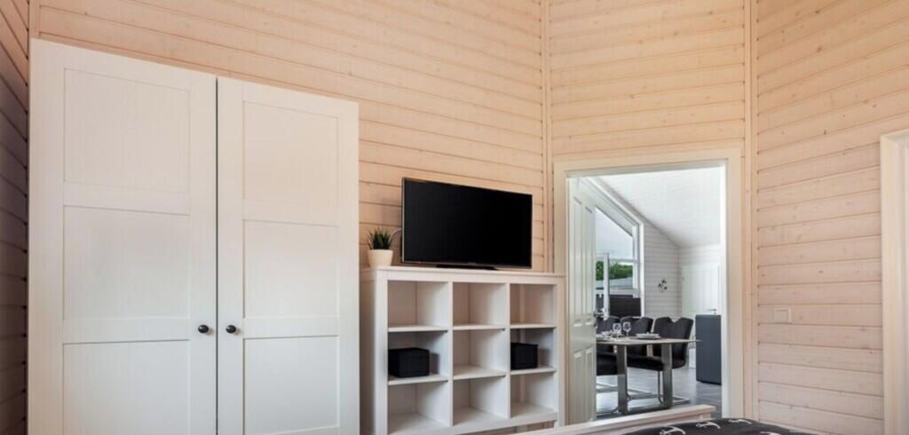 A room with a television on a shelf, a door, and a view into another room with a table and chairs.