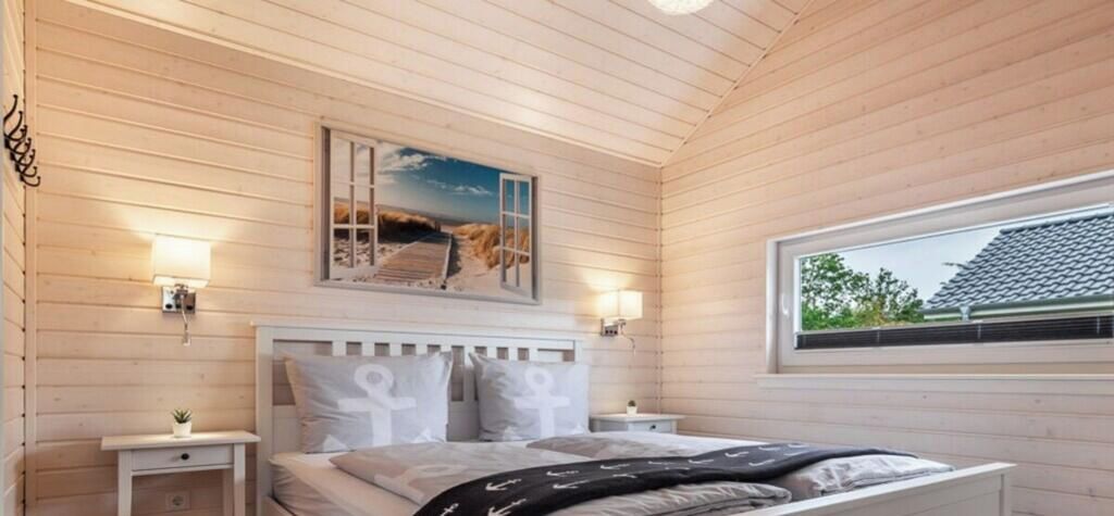 A bedroom with a wooden ceiling, a bed with white bedding, two bedside tables, a window, and a wall-mounted picture.