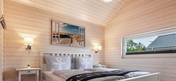 Ein Schlafzimmer mit Holzboden, einem Bett mit weißer Bettwäsche, zwei Nachttischen, einem Fenster und einem an der Wand hängenden Bild.