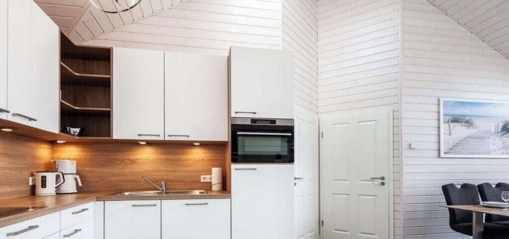 Una cocina moderna con armarios blancos, encimera de madera y horno empotrado.