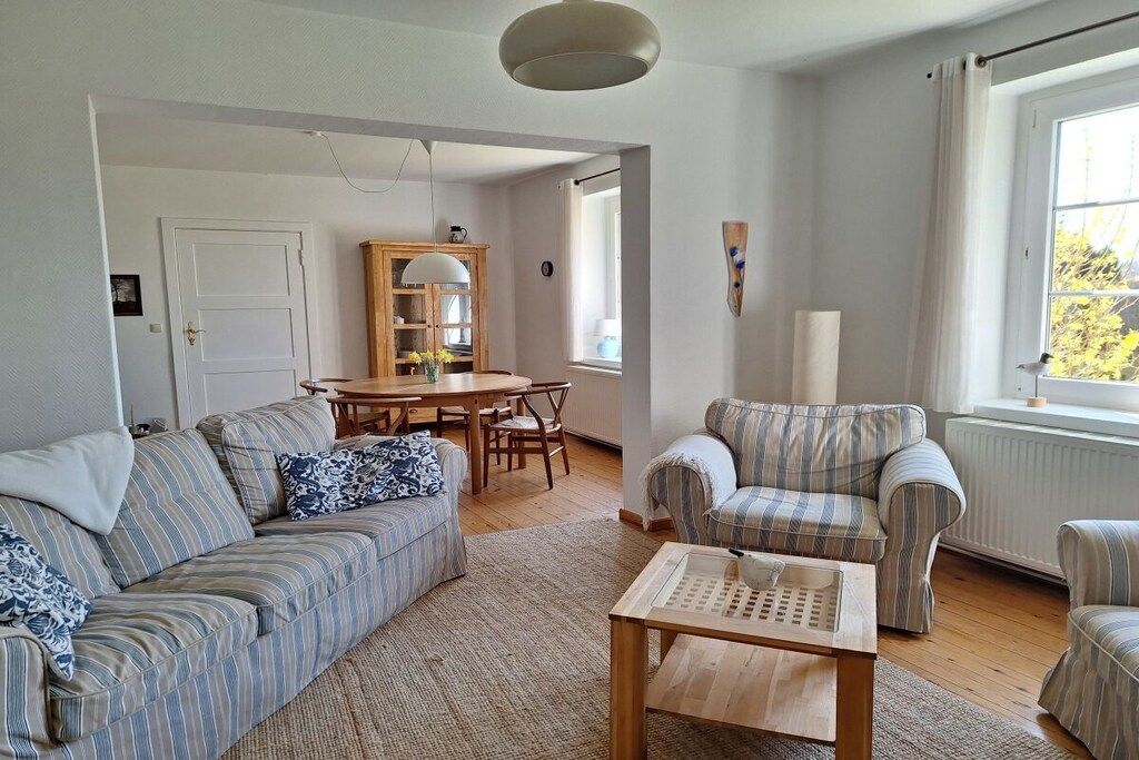 Ein Wohnzimmer mit einer Couch, Sesseln, einem Couchtisch und einem Esstisch mit Stühlen.