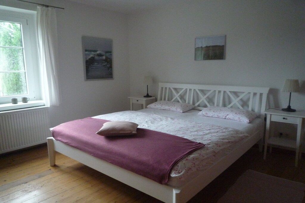 Ett sovrum med en säng, sängbord, ett fönster och ett element.