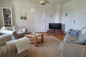 A living room with striped sofas, a television, a bookshelf, and a door. - Holiday home with 3 bedrooms (Wiek OT Woldenitz)