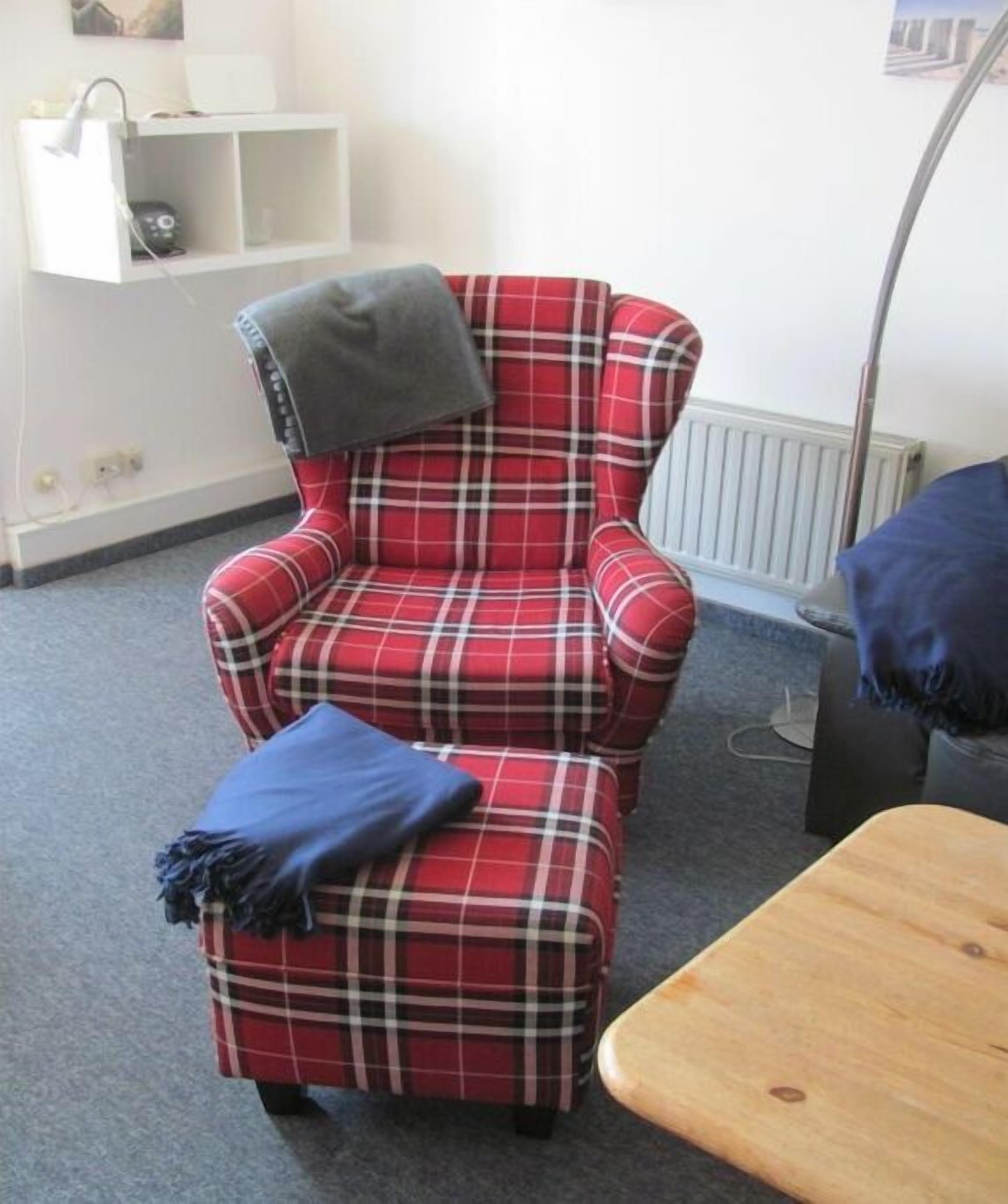 Ein gestreifter Ohrensessel mit einer Decke, ein Holztisch und ein weißes Regal mit Gegenständen.