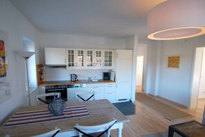 A modern kitchen with white cabinets, a dining table with chairs, and a large pendant light. - Stemsperle upper floor (Prerow)